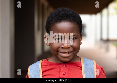 Smiling african american boy with backpack standing in school hallway, ready for class Stock Photo