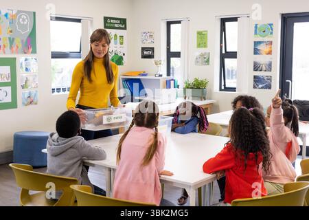 In school, female teacher discussing recycling with diverse students, engaging in learning Stock Photo
