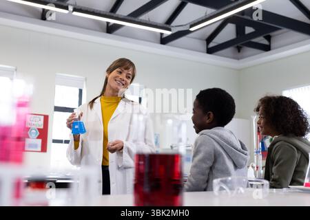 In school, female teacher demonstrating science experiment to engaged diverse students in classroom Stock Photo
