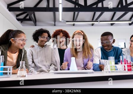 In school, diverse students conducting science experiment with female teacher, in safety goggles Stock Photo