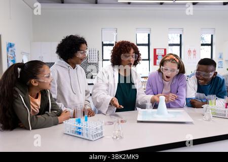 Diverse students in science class watching chemistry experiment with female teacher, at school Stock Photo