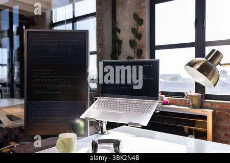 Laptop and monitor displaying code in modern office with natural light Stock Photo