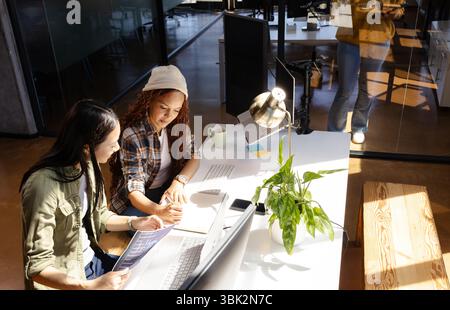 Diverse women collaborating on coding project at modern office desk with laptops Stock Photo