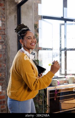Smiling woman writing code on glass board in modern office environment Stock Photo