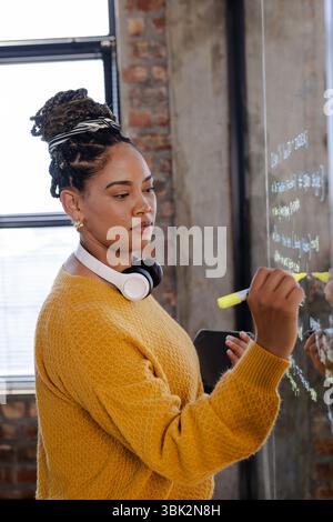 Woman in office writing code on glass board, focused and determined Stock Photo