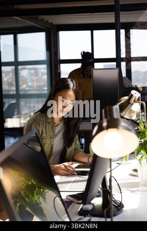 Asian woman coding on laptop in modern office, focused on work Stock Photo