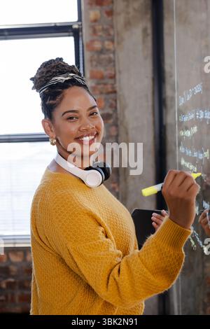 woman coding on glass board, smiling confidently in modern office Stock Photo
