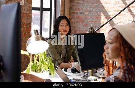 Diverse women collaborating on coding project at modern office, smiling and focused Stock Photo