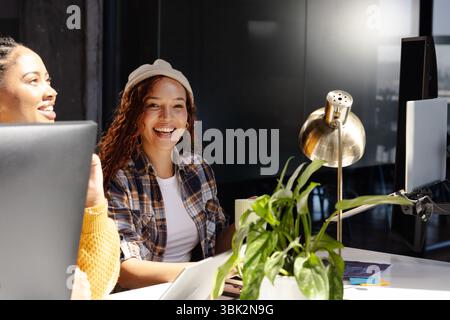 Diverse women collaborating on coding project at modern office, smiling and engaged Stock Photo
