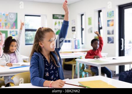 Diverse students raising hands in classroom, eager to participate in school lesson Stock Photo