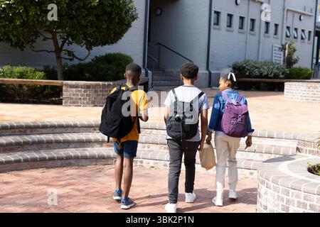 diverse students walking together on school campus with backpacks Stock Photo
