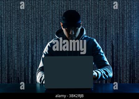 Cyber attack. Hacker working on laptop at table. Digital code behind him Stock Photo