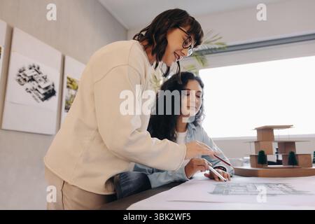 Two female professionals collaborate while analyzing building plans in an office environment, fostering teamwork and creativity. The workspace reflect Stock Photo