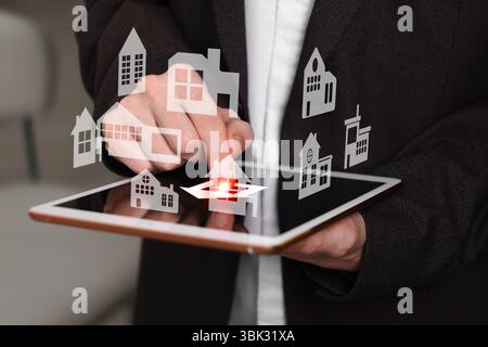 Real estate agent looking for housing via tablet indoors, closeup. Illustrations of different buildings over device Stock Photo
