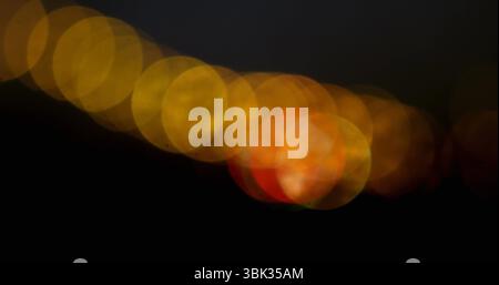 Showing overlapping bokeh lights moving diagonally across black background, featuring reddish orb Stock Photo