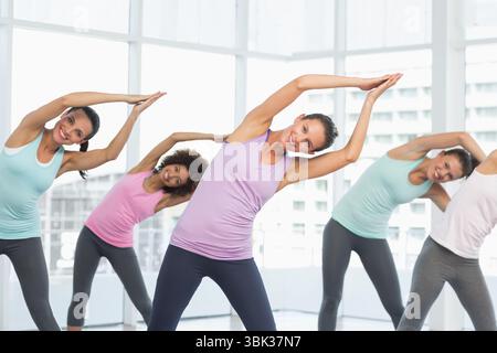 Fitness women in pastel attire are doing synchronized side bends in flat studio with urban skyline Stock Photo