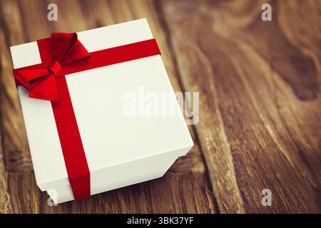White gift box wrapped with red satin ribbon is sitting on rustic wooden table, flat design Stock Photo