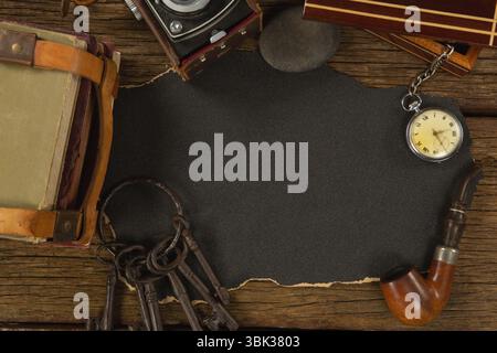 Overhead flat design showing torn dark paper on rustic wood, featuring books, camera, pipe, keys Stock Photo
