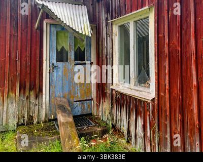 Blue door on a old abandoned red wooden cottage in bad condition Stock Photo