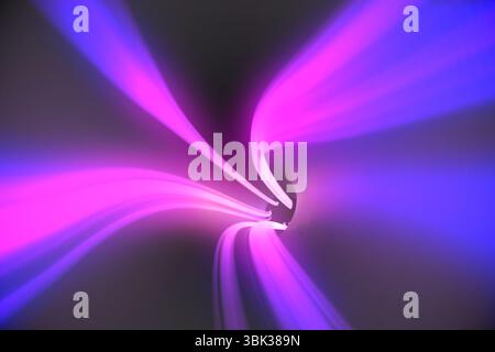 Swirling neon pink and blue light trails are twisting and converging in muted gray abstract space Stock Photo