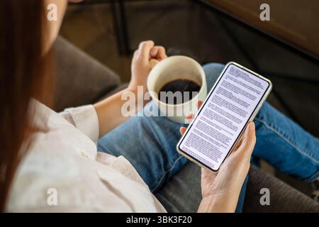 woman hand holding coffee cup and phone, reading text on mobile screen for digital press article feed in the morning. mockup media publication website Stock Photo