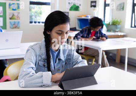 In classroom, focused girl using tablet for learning, engaged in schoolwork Stock Photo