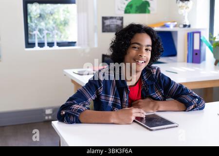 In school, boy using tablet in classroom, smiling and focused on learning Stock Photo