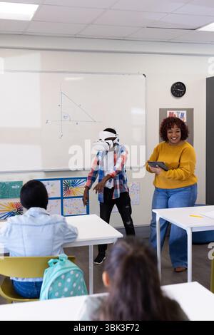 African american boy using vr headset in classroom while female teacher observes, at school Stock Photo