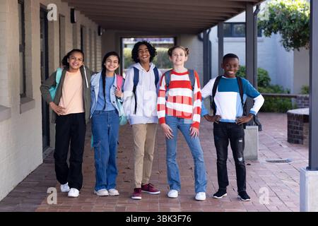 Diverse group of students standing together outside school, smiling with backpacks Stock Photo