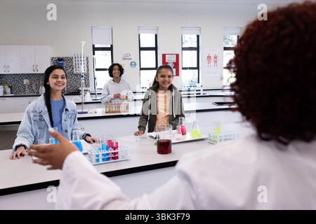 Diverse students in science class engaging with female teacher, surrounded by test tubes, at school Stock Photo