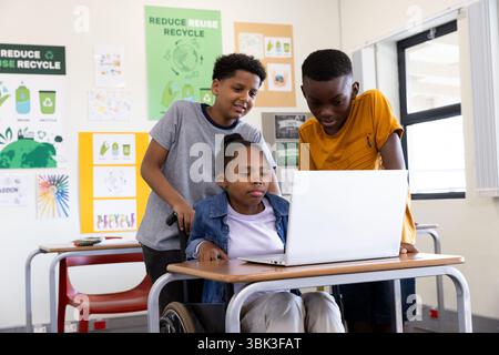 Diverse students collaborating on laptop in classroom, engaged in recycling project, at school Stock Photo