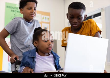 Diverse students collaborating on laptop in classroom, focused on group project, at school Stock Photo