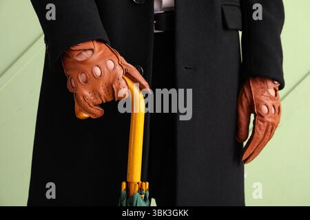 Man in stylish brown leather gloves with umbrella on green background, closeup Stock Photo