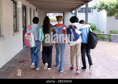 Diverse group of students walking together at school, carrying colorful backpacks Stock Photo