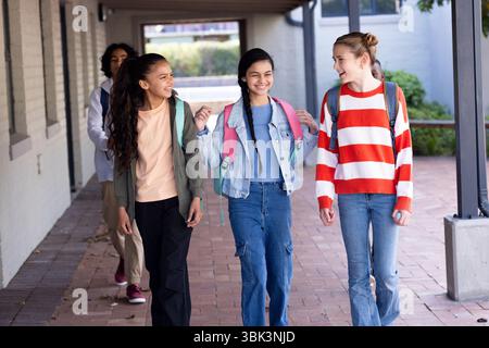 Diverse students walking together outside school, smiling and chatting with backpacks Stock Photo