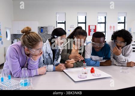 In school, diverse students wearing safety goggles conducting science experiment in classroom Stock Photo