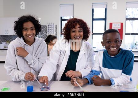 Science female teacher and diverse students experimenting with colorful liquids in school lab Stock Photo