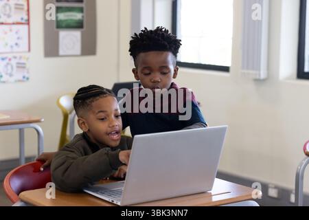 School diverse boys using laptop together in classroom, collaborating on project Stock Photo