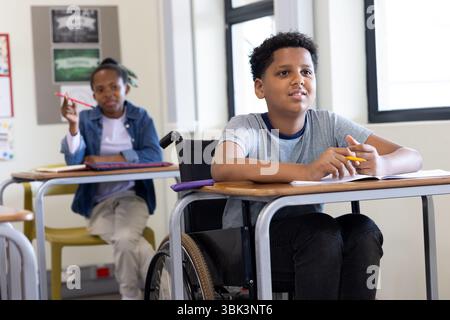 Diverse students in classroom engaged in learning, boy in wheelchair participating, at school Stock Photo