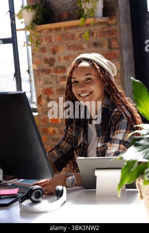 Smiling woman coding at desk in modern office with natural light Stock Photo