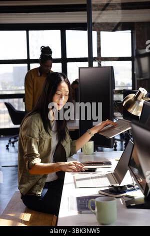 Asian woman coding on laptop in modern office, focused on work Stock Photo