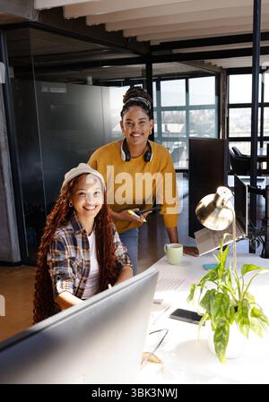 Diverse women collaborating in modern office, smiling and using computer for coding project Stock Photo