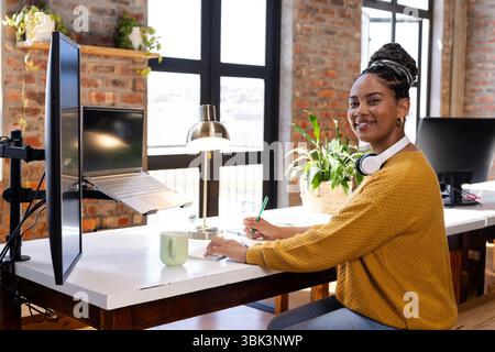 Smiling woman coding on laptop at office desk with headphones and coffee Stock Photo