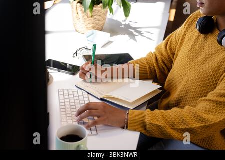 Woman coding at desk, writing notes in notebook, focused on work, at office Stock Photo