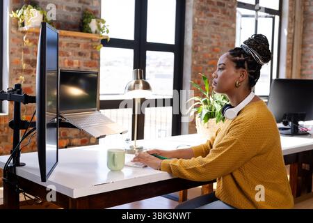 Coding on laptop at modern office desk, woman focused and determined Stock Photo