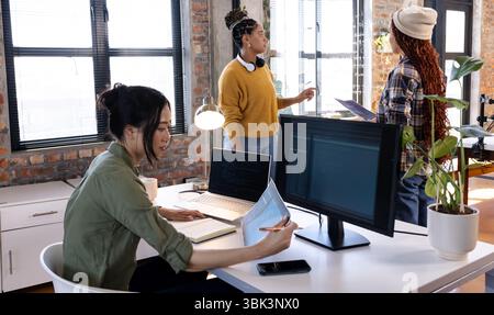 Collaborating on software, diverse women using laptops and monitors in modern office Stock Photo