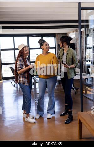 Diverse women in office collaborating on coding project with laptops, smiling Stock Photo