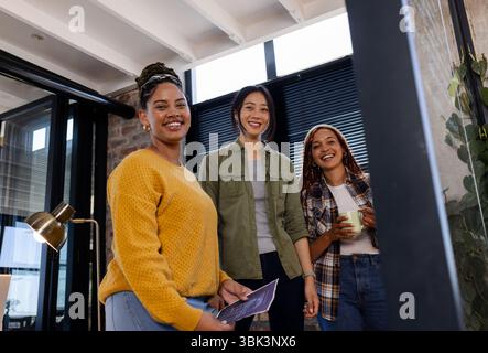 Diverse women in modern office collaborating on tech project, smiling confidently Stock Photo