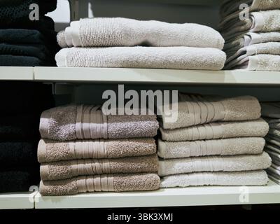 White and tan stack of towels sits on a shelf next to a black stack. The white towels are folded neatly and the black towels are piled on top of them. Stock Photo
