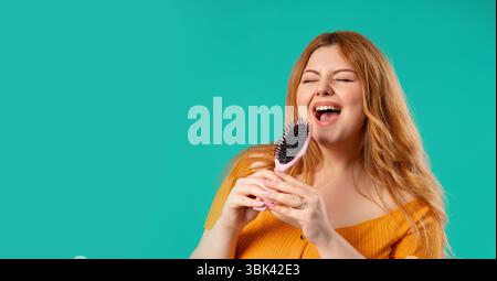 Body positive woman Singing, Dancing With Hair Brush Instead Microphone On Blue  Stock Photo